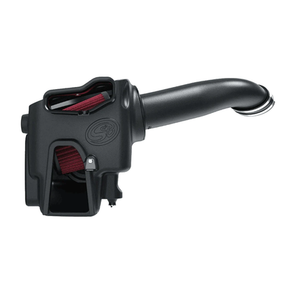 S&B Filters cold air intake kit designed for a Ford 6.7L Powerstroke diesel engine, featuring a matte black enclosed airbox with a clear plastic inspection lid on top revealing a large red pleated air filter inside, connected to a long, curved black intake tube fitted with heavy-duty mounting hardware and couplers.